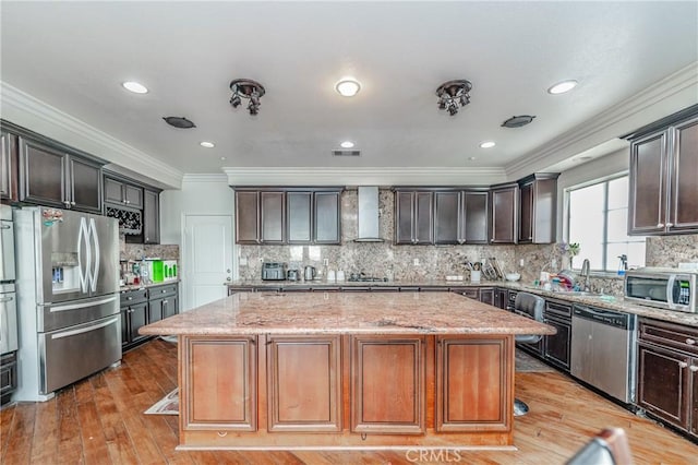 kitchen featuring stainless steel appliances, light stone countertops, wall chimney exhaust hood, and a center island