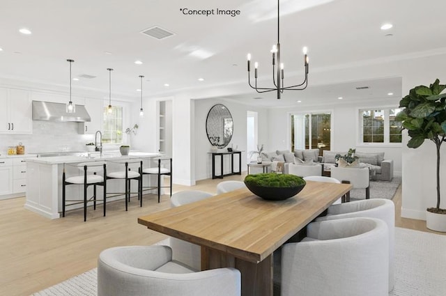 dining area with light wood-type flooring, an inviting chandelier, ornamental molding, and sink