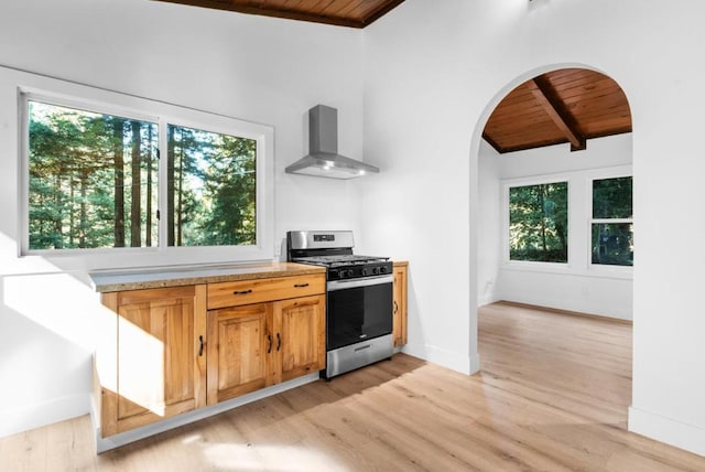 kitchen featuring vaulted ceiling with beams, wall chimney exhaust hood, wood ceiling, gas stove, and light hardwood / wood-style flooring