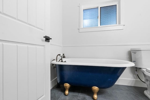 bathroom with tile patterned flooring, a tub to relax in, and toilet