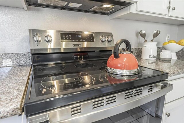 details with wall chimney range hood, stainless steel range with electric cooktop, and white cabinets