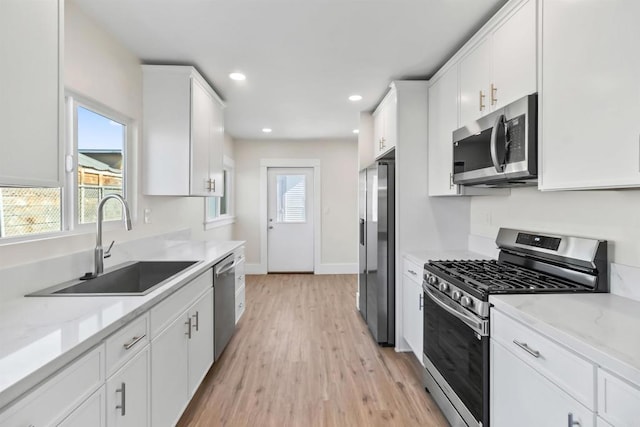 kitchen featuring appliances with stainless steel finishes, white cabinets, light stone countertops, and sink