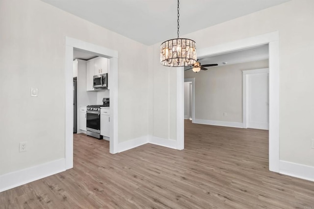 unfurnished dining area featuring ceiling fan with notable chandelier and hardwood / wood-style floors