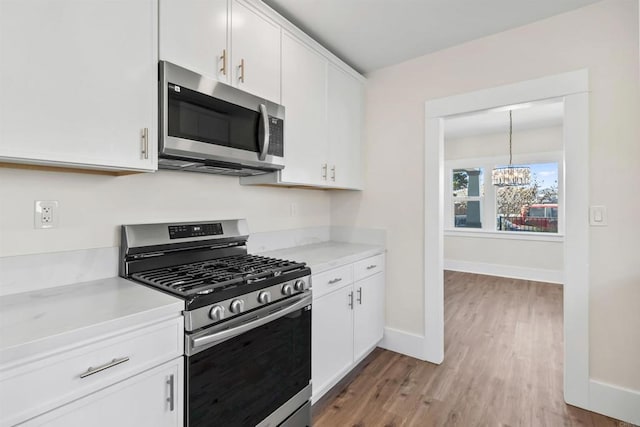 kitchen with white cabinets, light hardwood / wood-style floors, hanging light fixtures, a chandelier, and appliances with stainless steel finishes