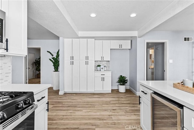 kitchen with white cabinetry, beverage cooler, tasteful backsplash, black range with gas cooktop, and light hardwood / wood-style floors