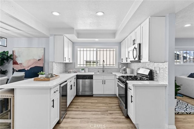 kitchen with white cabinets, sink, a textured ceiling, kitchen peninsula, and stainless steel appliances