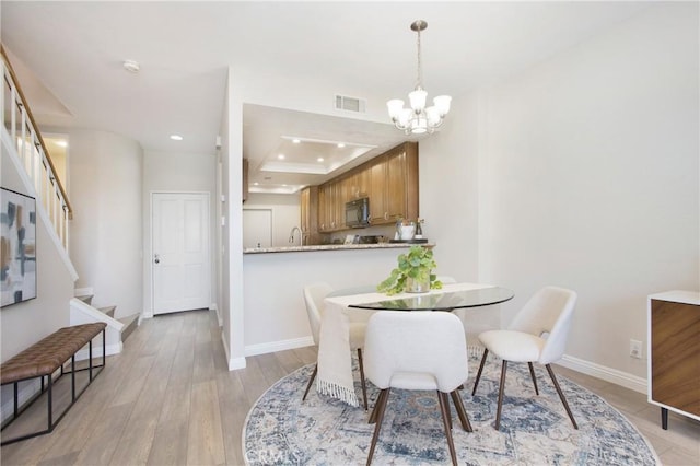 dining room with an inviting chandelier, a raised ceiling, and light hardwood / wood-style flooring