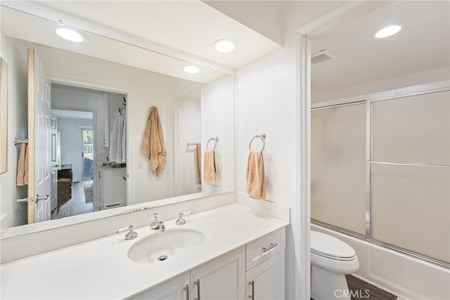 full bathroom with wood-type flooring, bath / shower combo with glass door, vanity, and toilet