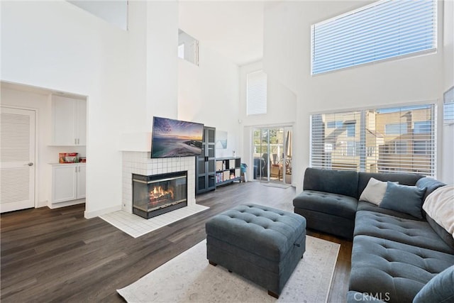 living room with a high ceiling, a tile fireplace, and dark hardwood / wood-style floors