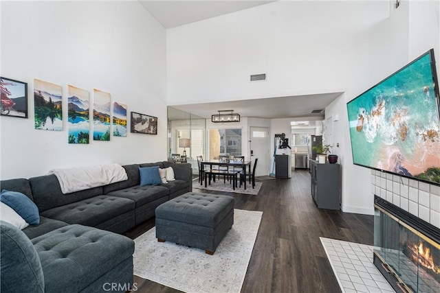 living room featuring a towering ceiling, a tile fireplace, and dark wood-type flooring