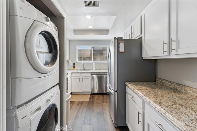 laundry room featuring dark wood-type flooring, stacked washer and clothes dryer, and sink