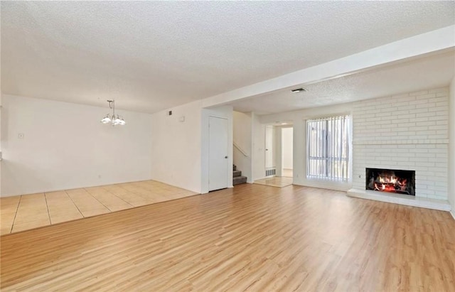 unfurnished living room featuring a brick fireplace, an inviting chandelier, a textured ceiling, and light hardwood / wood-style floors