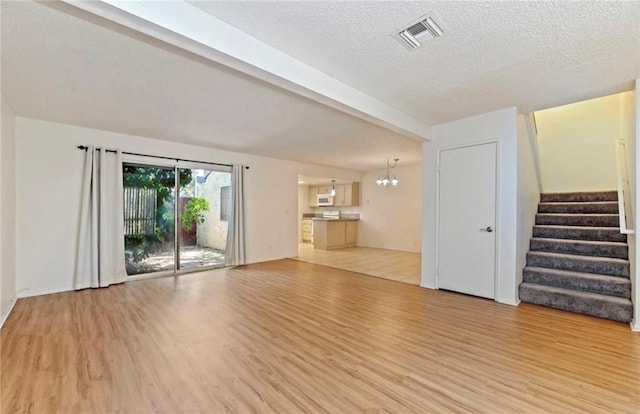 unfurnished living room featuring light hardwood / wood-style floors, a textured ceiling, and a notable chandelier