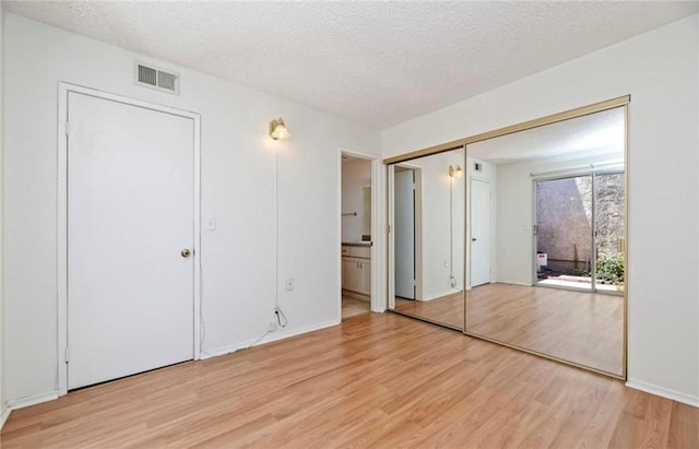 unfurnished bedroom featuring ensuite bath, a closet, a textured ceiling, and light hardwood / wood-style floors