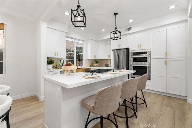 kitchen with a kitchen island, white cabinets, hanging light fixtures, and appliances with stainless steel finishes