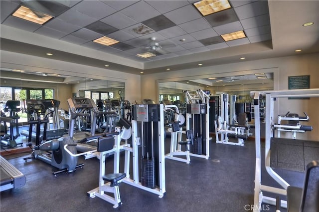 exercise room with ceiling fan, a drop ceiling, and a tray ceiling