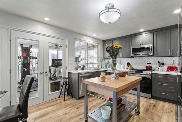 kitchen with french doors, sink, stainless steel appliances, backsplash, and light wood-type flooring