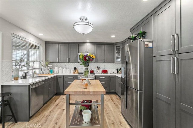 kitchen featuring appliances with stainless steel finishes, tasteful backsplash, gray cabinetry, sink, and light hardwood / wood-style floors