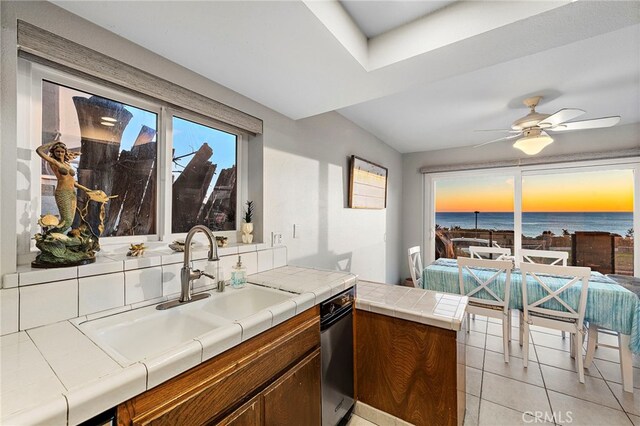 kitchen featuring tile countertops, a water view, a sink, decorative backsplash, and brown cabinetry