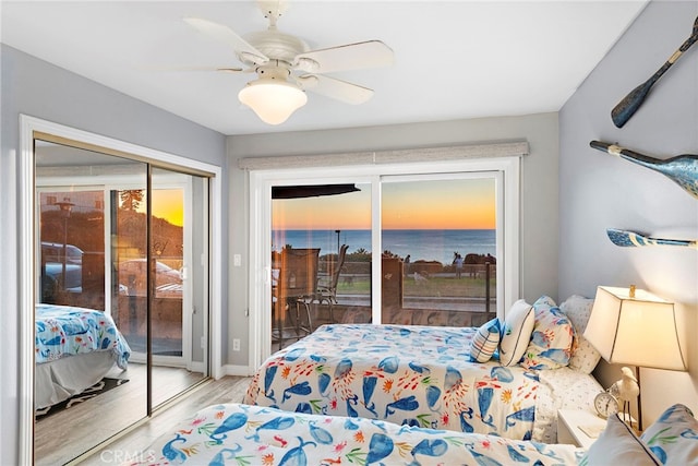 bedroom with baseboards, a ceiling fan, wood finished floors, a water view, and access to outside