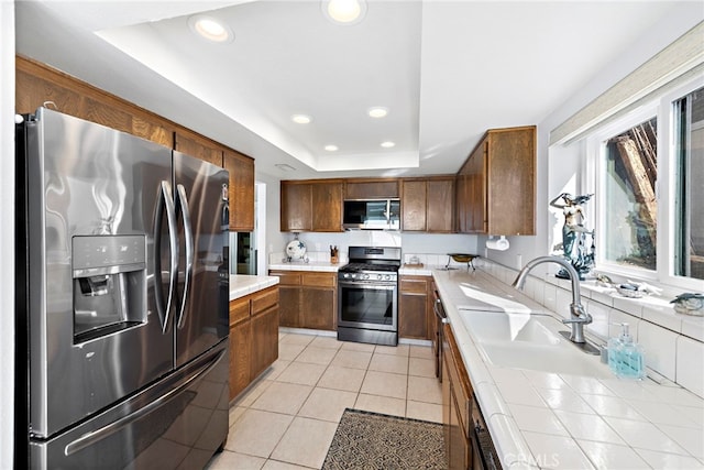 kitchen with light tile patterned floors, a tray ceiling, stainless steel appliances, a sink, and recessed lighting