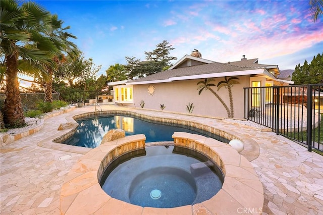 pool at dusk featuring an in ground hot tub and a patio area