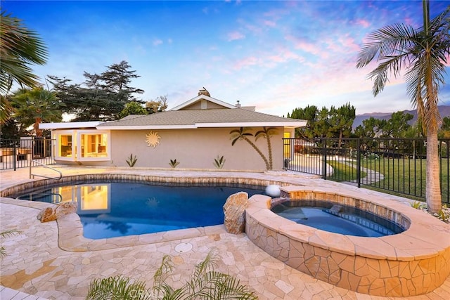 pool at dusk featuring a patio and an in ground hot tub