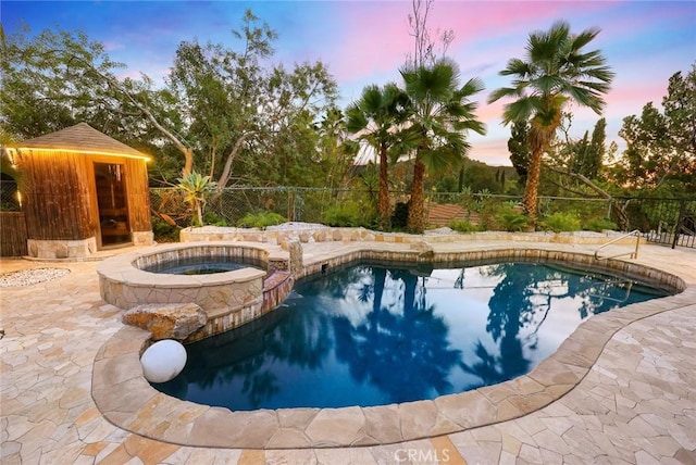 pool at dusk with a patio and an in ground hot tub