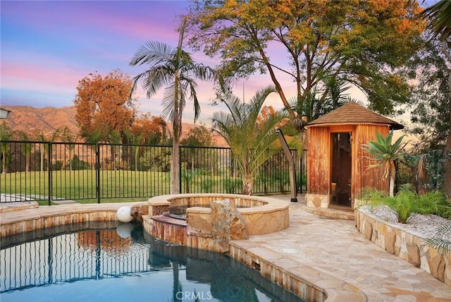 pool at dusk featuring a mountain view, a yard, and an in ground hot tub