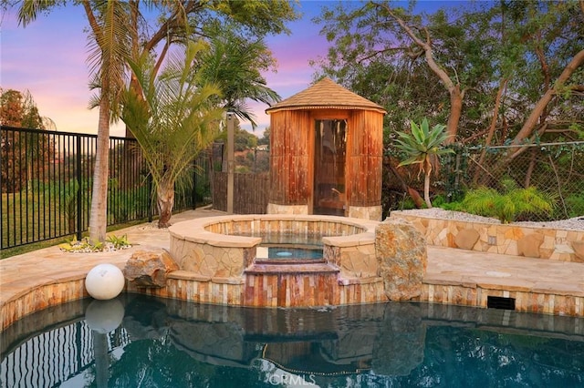 pool at dusk featuring an in ground hot tub