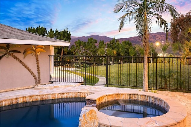 patio terrace at dusk with a swimming pool with hot tub, a mountain view, and a yard