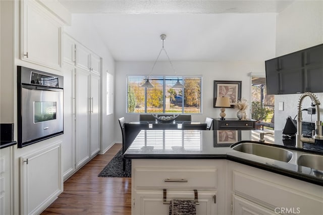 kitchen featuring dark wood-type flooring, sink, white cabinetry, hanging light fixtures, and oven