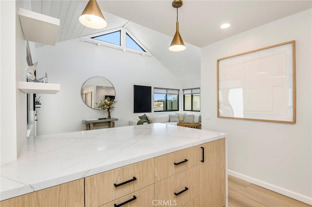 kitchen with light stone counters, light hardwood / wood-style flooring, lofted ceiling, decorative light fixtures, and light brown cabinetry