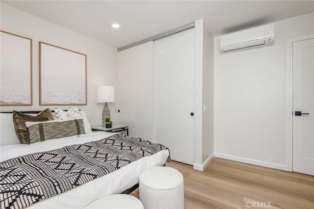 bedroom with a wall mounted air conditioner, light wood-type flooring, and a closet