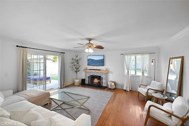 living room featuring a tile fireplace, hardwood / wood-style flooring, ceiling fan, and crown molding