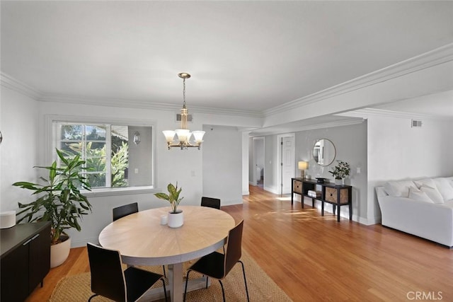 dining room with light wood-type flooring, ornamental molding, and a chandelier