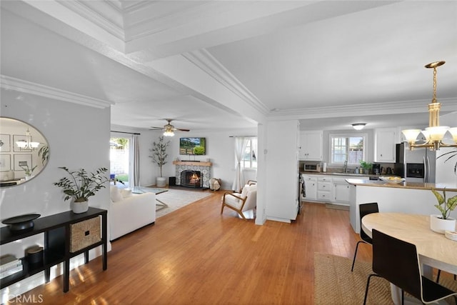 dining room with ceiling fan with notable chandelier, sink, light hardwood / wood-style flooring, ornamental molding, and a fireplace