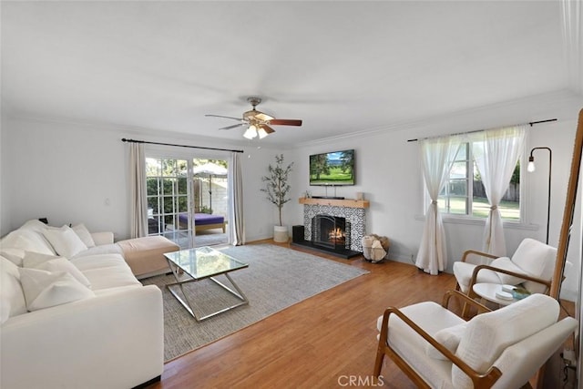 living room with a tile fireplace, wood-type flooring, ceiling fan, and a healthy amount of sunlight