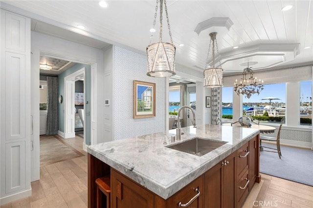 kitchen featuring a kitchen island with sink, sink, a water view, a chandelier, and light hardwood / wood-style floors