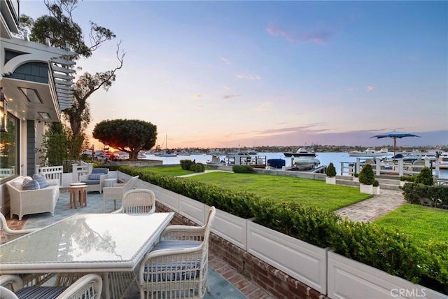 patio terrace at dusk featuring a water view and a lawn