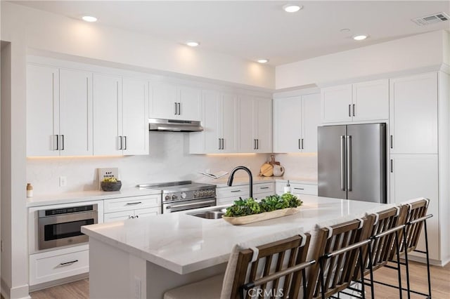 kitchen featuring a center island with sink, a kitchen breakfast bar, sink, premium appliances, and light stone counters