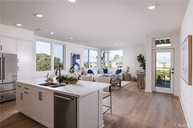 kitchen featuring appliances with stainless steel finishes, light wood-type flooring, a kitchen island with sink, sink, and white cabinetry