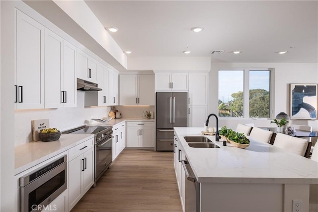 kitchen featuring a breakfast bar, premium appliances, a kitchen island with sink, sink, and white cabinetry