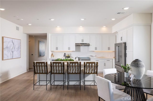 kitchen with a breakfast bar, dark hardwood / wood-style flooring, white cabinetry, and high quality fridge