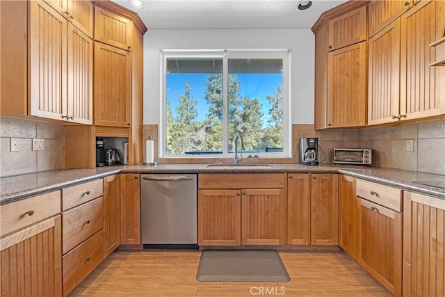 kitchen with dark stone countertops, stainless steel dishwasher, decorative backsplash, sink, and light wood-type flooring