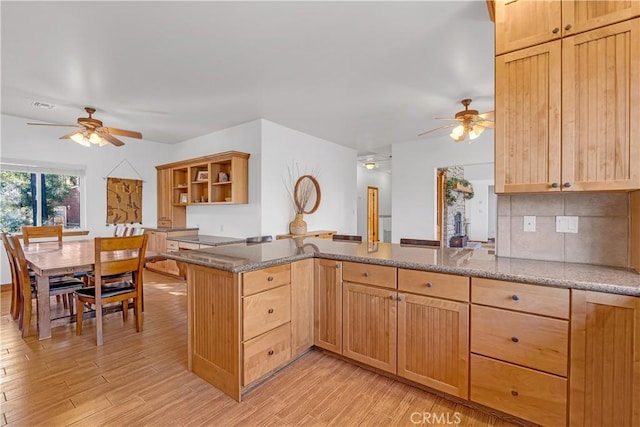 kitchen with ceiling fan, backsplash, kitchen peninsula, light wood-type flooring, and light stone counters