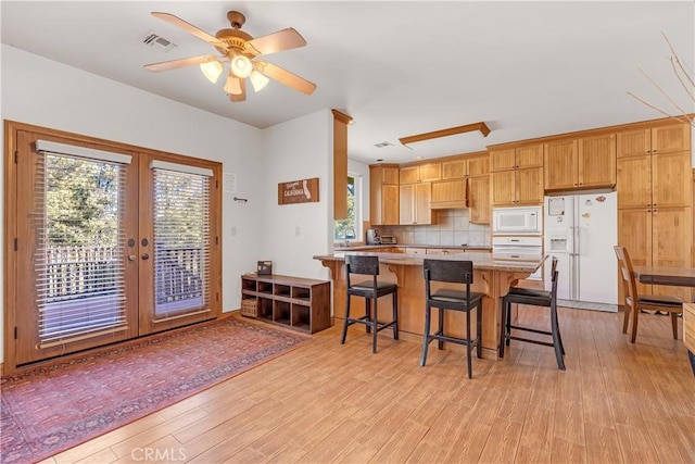 kitchen with ceiling fan, decorative backsplash, white appliances, light hardwood / wood-style flooring, and a breakfast bar area