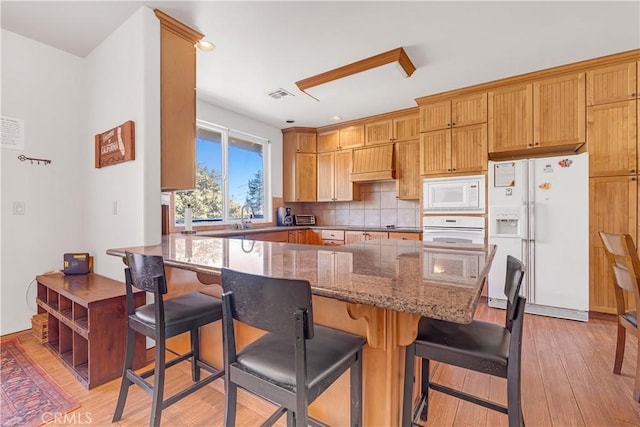 kitchen featuring a breakfast bar, white appliances, kitchen peninsula, and stone counters