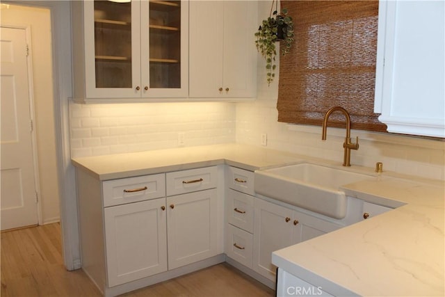 kitchen with decorative backsplash, light stone counters, white cabinetry, and sink