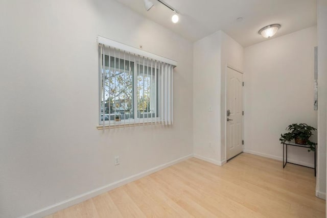 empty room with track lighting and light hardwood / wood-style floors